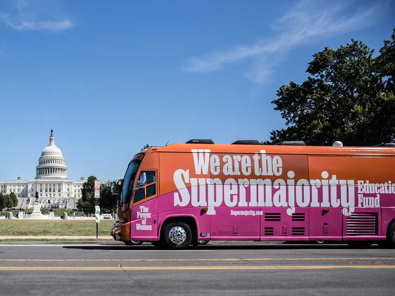 A bus with the words "We are the Supermajority" is on a street in front of the United States Capitol building