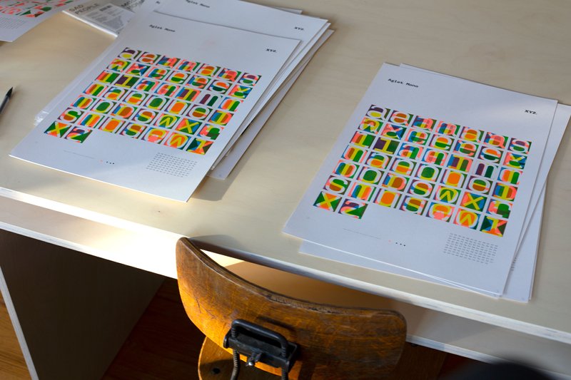Two stacks of colorful art prints rest on a wooden table with a chair.
