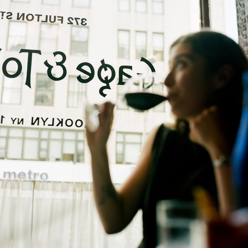 A person drinking wine in front of a window with the Gage & Tollner logo