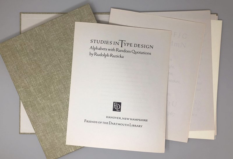 A folded paper with the title "Studies in Type Design" rests on a cloth portfolio and other papers