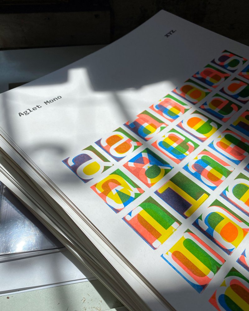 A stack of colorful art prints rest on a table with dramatic shadows.