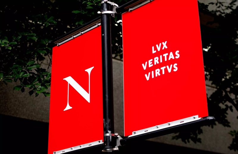 The Northeastern N monogram and motto appear on red banners on a pole