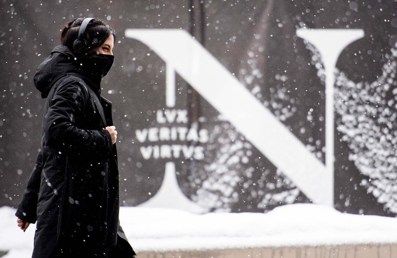 A person in winter clothing walks in front of a large image of the Northeastern N monogram and motto